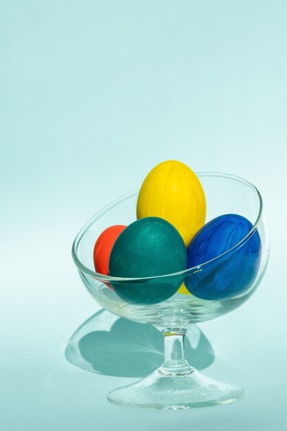 Uova di pasqua colorate dipinte a mano in un vaso di vetro trasparente contro una superficie azzurra, cornice verticale, spazio copia, primo piano. felice pasqua concetto.