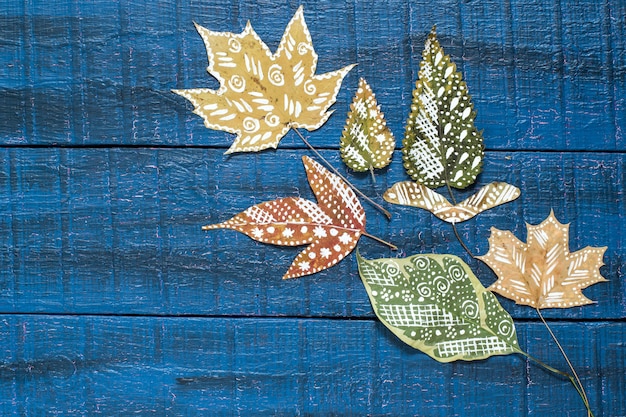 テキスト用のスペースと青い木の表面の乾燥した紅葉に手描き