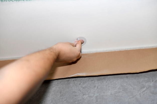 Рука маляра, шлифующего дефекты потолка, чтобы нанести второй слой краски.