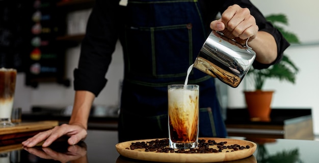カフェで木製の皿にコーヒー飲み物にミルクを注ぐ人の手 タイ 選択的な焦点