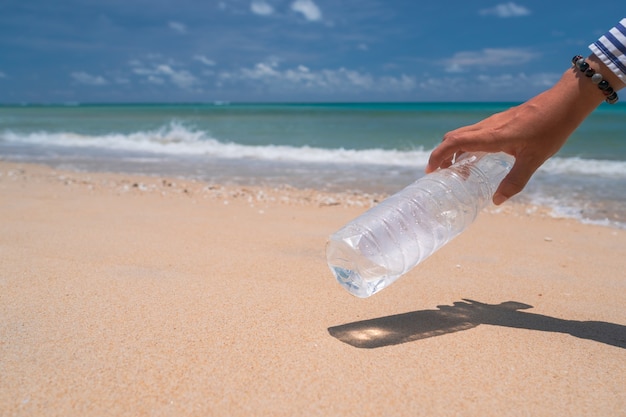 Hand pick up empty water bottle or trash at beautiful beach. Environment Global warming issue.