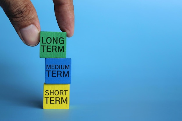 Hand pick wooden cube with text long term on blue background with copy space investment concept