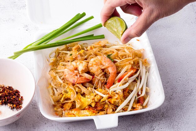 Hand picking lemon and squeezing it to cook Fried noodle Thai style with prawns in foam box and. Pad Thai with vegetables. popular street food of Thailand.