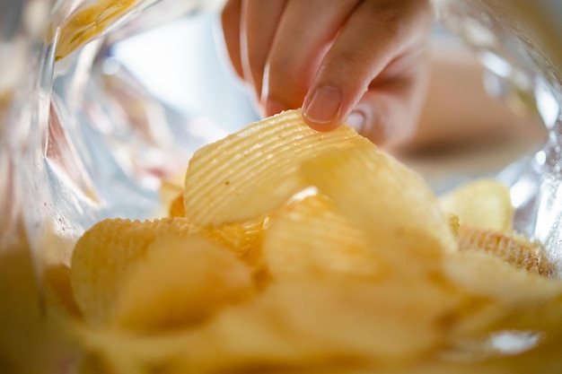 Hand picking potato chips inside snack bag