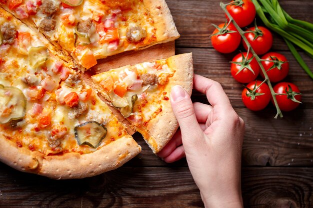 Hand picking tasty slice of pizza lying on wooden table, Focused on hand.