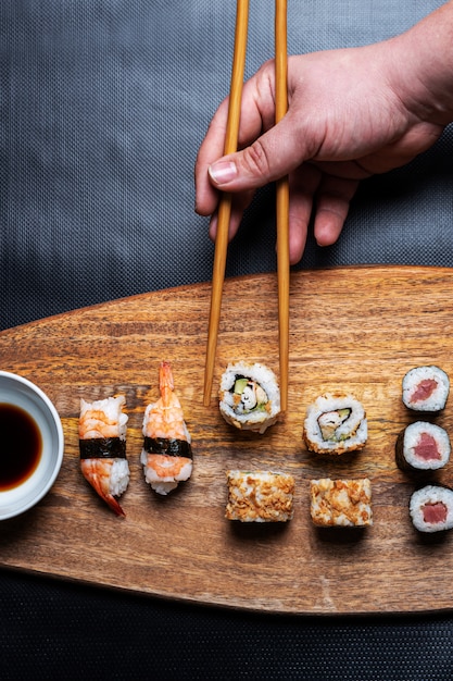 hand picking up sushi Roll from wooden board. Maki, Nigiri and California Roll sushi composition with chopsticks and soy sauce.