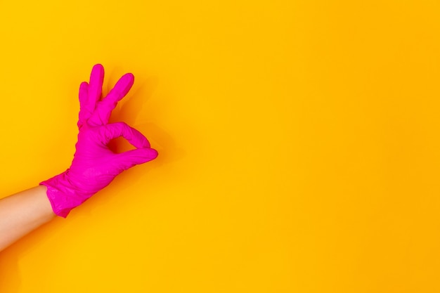 Hand in pink rubber glove showing nice sign isolated on yellow studio background with copyspace