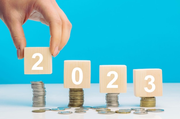 Hand place wooden cube 2023 with stack of coins with blue background and copy space Saving money and financial plan concept for investment in new year 2023