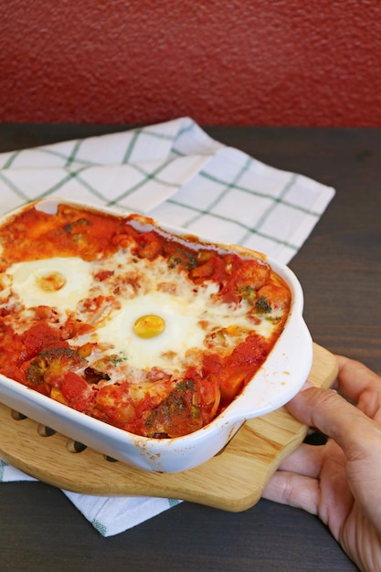 Hand Placing a Bowl of Freshly Cooked Shakshouka on the Kitchen Table