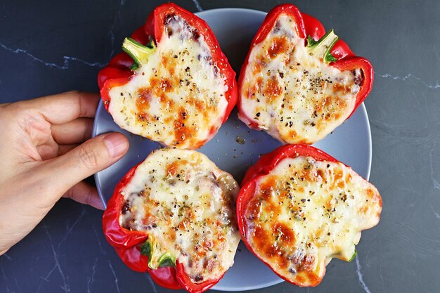 Hand Placing a Plate of Delectable Homemade Stuffed Bell Peppers on Black Marble Table