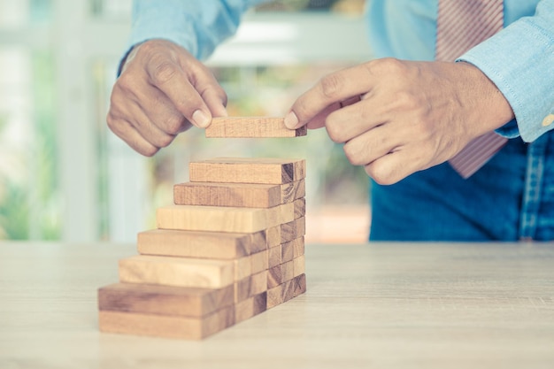 Hand placing wood block tower stack in pyramid stair step