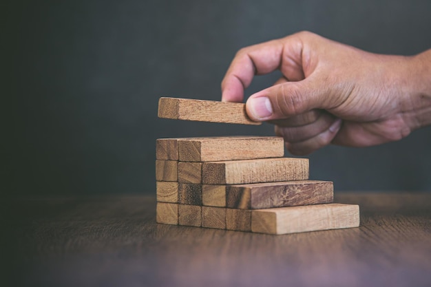 Hand placing wood block tower stack in pyramid stair step