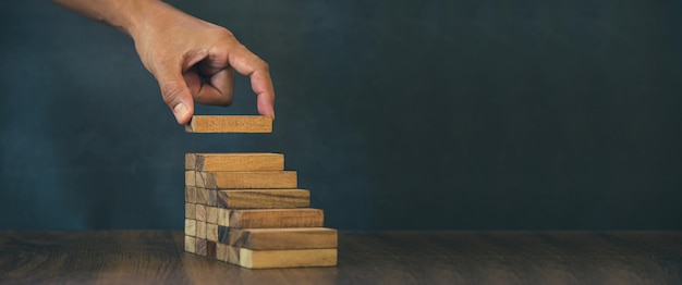 Hand placing wood block tower stack in pyramid stair step