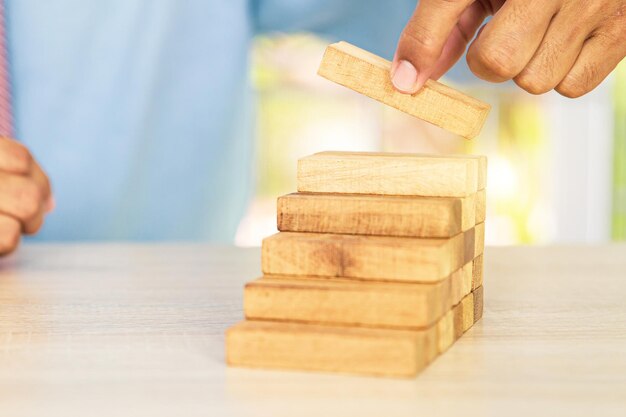Photo hand placing wooden block tower stack in pyramid stair step with caution to prevent collapse or crash concepts of financial risk management and strategic planning and business challenge plan