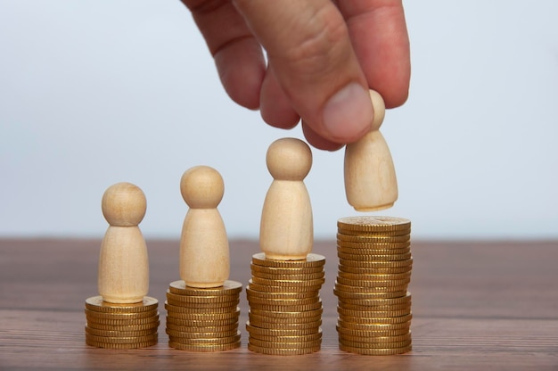Hand placing wooden people figure on top of gold coins goal\
achievement business growth and career progression