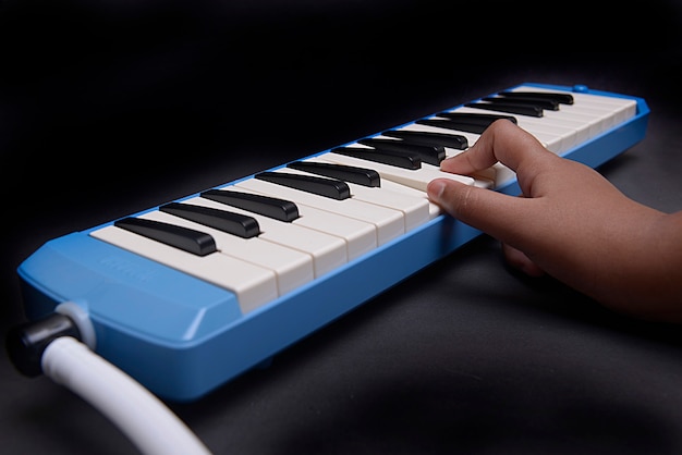 Hand playing pianica blow-organ musical instrument with black background