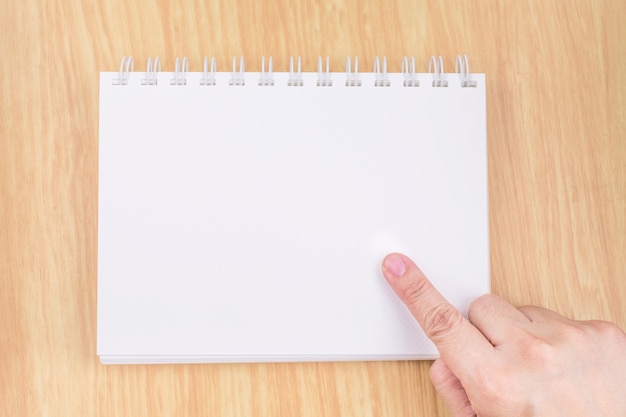 Hand point to blank white notebook on wood table top