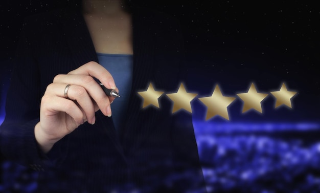 Hand pointing five star symbol to increase rating of company.\
hand holding digital graphic pen and drawing digital hologram five\
stars sign on city dark blurred background.