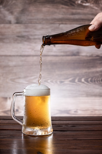 Hand pouring beer into a cold jug on wooden base.