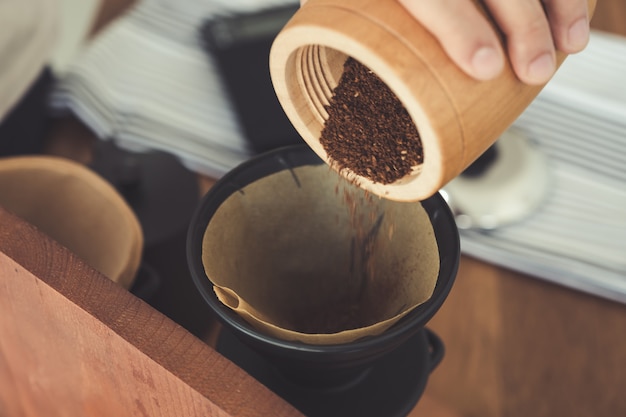 A hand pouring coffee from wooden grinder into filter