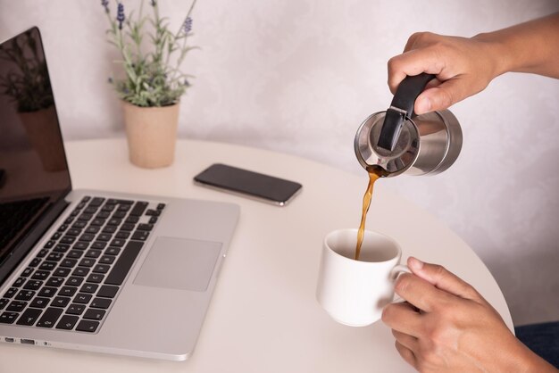 Photo hand pouring a coffee in front of the computer