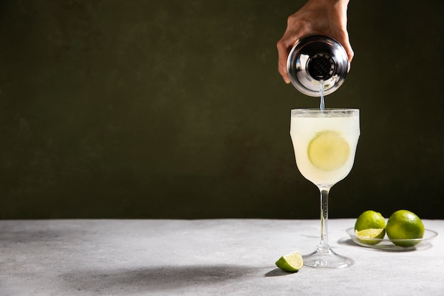 Hand pouring daiquiri in glass with lime