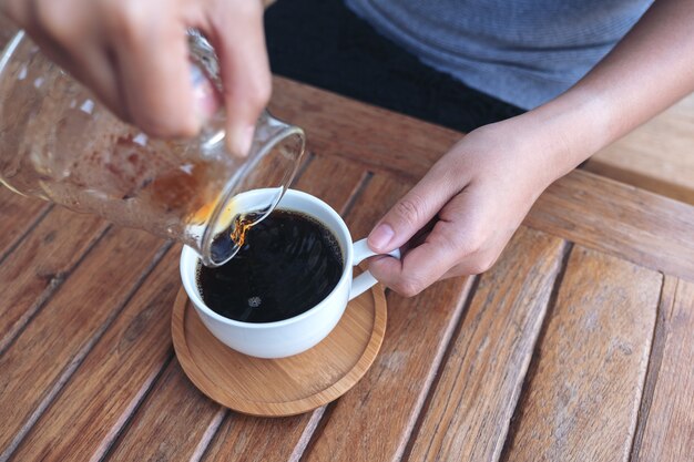 hand pouring drip coffee into a white mug on vintage wooden table