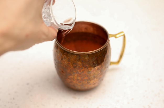 A hand pouring a glass of moscow mule from a copper mug.