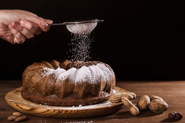 Photo hand pouring icing sugar on top of a delicious chocolate sponge cake