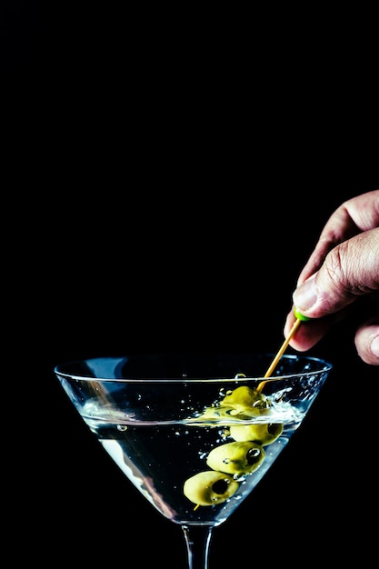 Hand pouring some olives into a martini glass. Vertical orientation. Copyspace.