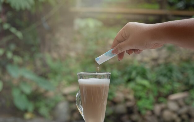 コーヒーのカップで砂糖を注ぐ手。