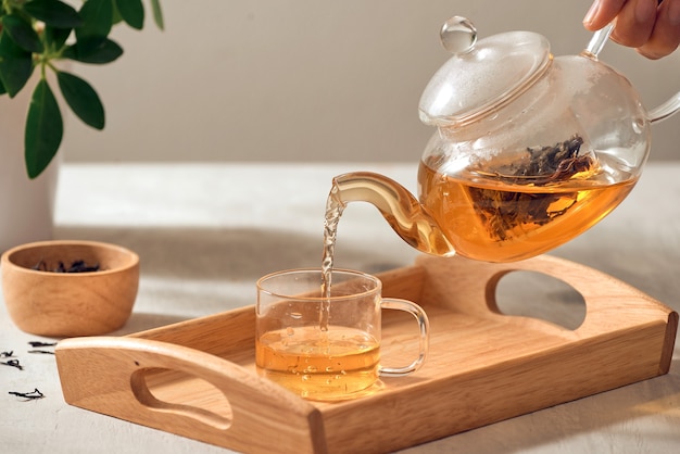 Photo a hand pouring tea from glass teapot on wooden serving tray