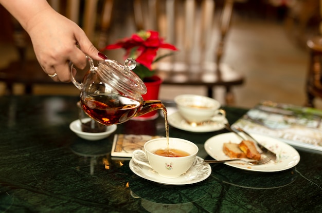 背景をぼかしでティーポットからカップにお茶を注ぐ手。