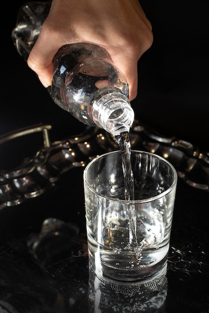 La mano versa acqua fresca e pulita da una bottiglia di plastica in un bicchiere. uno stile di vita sano