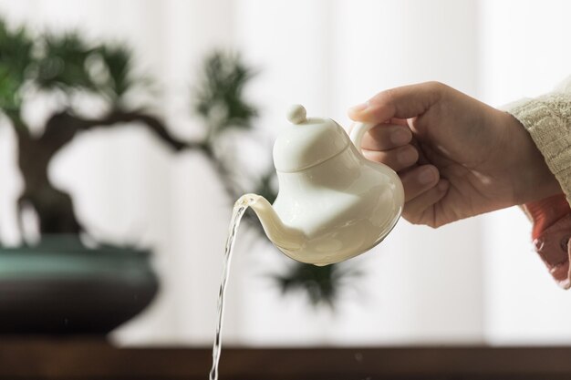 A hand pours a teapot from a teapot into a pot.