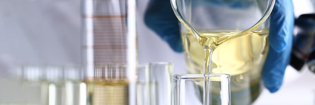 Hand pours yellow liquid into test tube closeup