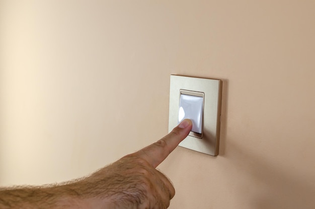 Hand pressing button of a light switch to turn light on or off