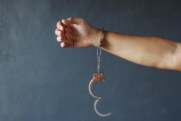 Hand of prisoner man wearing orange clothes with handcuffs isolated over grey background Free from