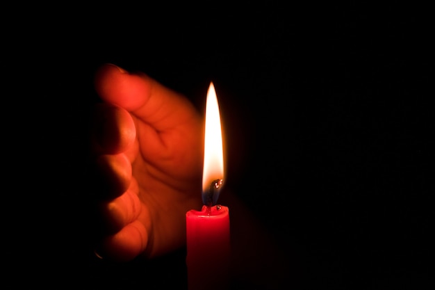 Hand protecting candle light from the wind in darkness on black background