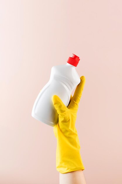 Hand in protective glove holds blank bottle of detergent on beige close view