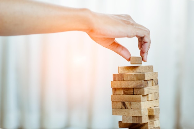 Hand  pulling out or placing wood block on the tower in modern office. plan and strategy in business. blur for background.