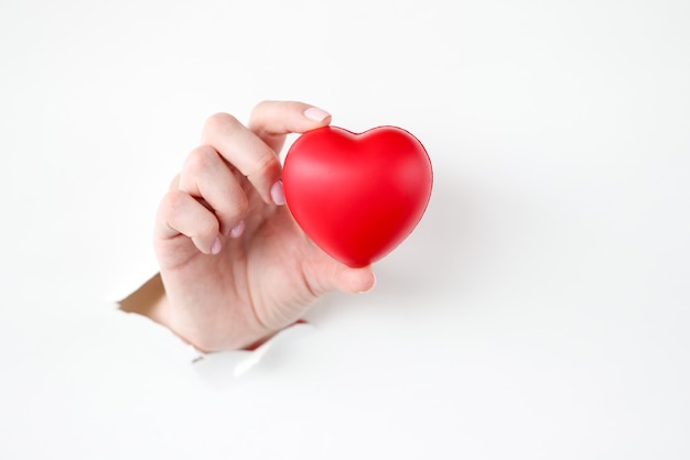 Рука вытаскивает игрушку красное сердце из рваной бумаги