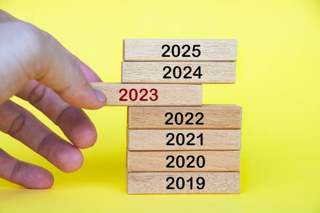 Hand pulling out year 2023 text on wooden blocks Year to year progress concept