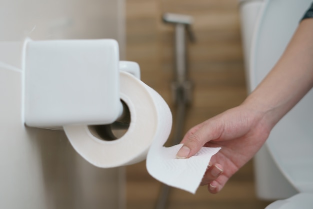 Hand pulling a roll of toilet paper tissue.