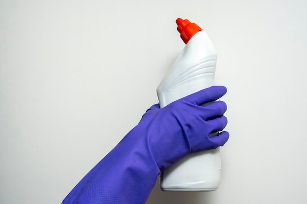 A hand in a purple rubber cleaning glove holds a plastic bottle of detergent on a white background