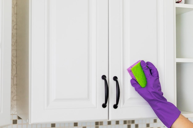 Hand in a purple rubber glove cleaning white kitchen cabinet