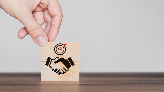 Hand put a handshake icon on wooden cube block, Business partner or mergers and acquisition concept.