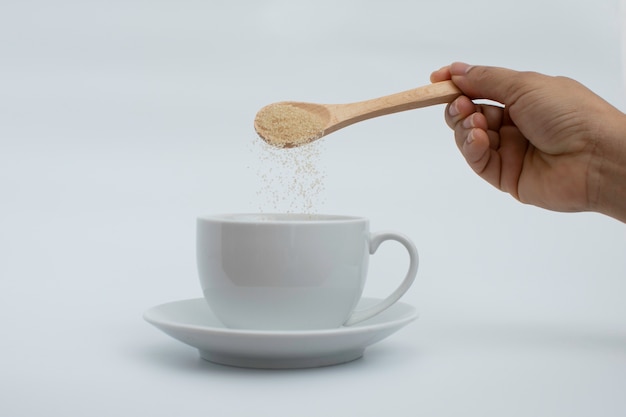 Hand put wooden spoon of sugar in white hot drink cup