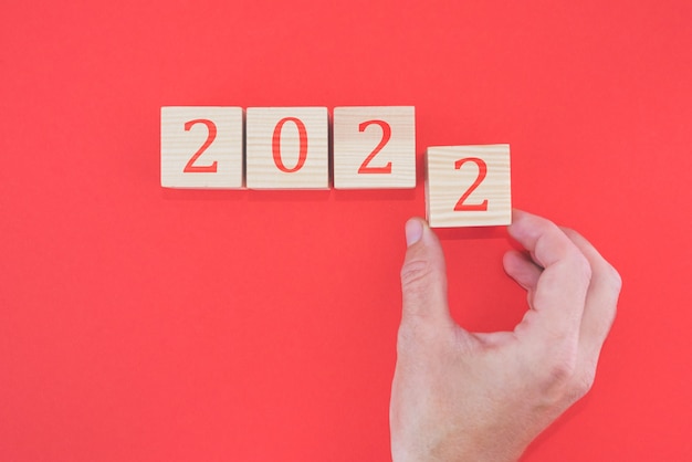 Hand puts block from 2022 on red background. New year concept. 2022 on wood cubes