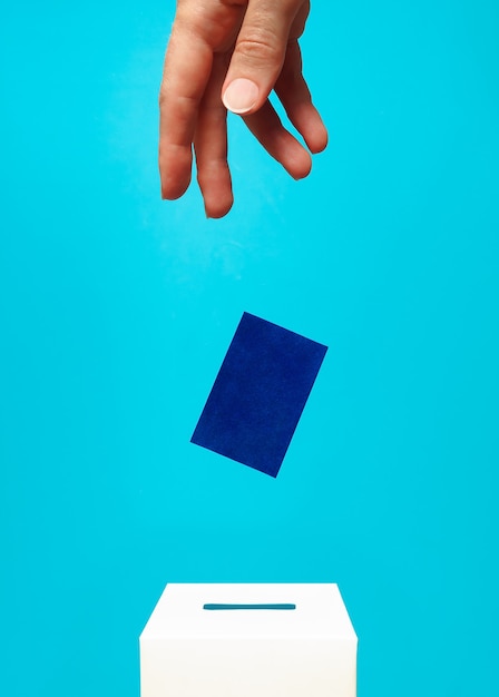 рука кладет синюю карточку в белую урну для голосования с прорезью